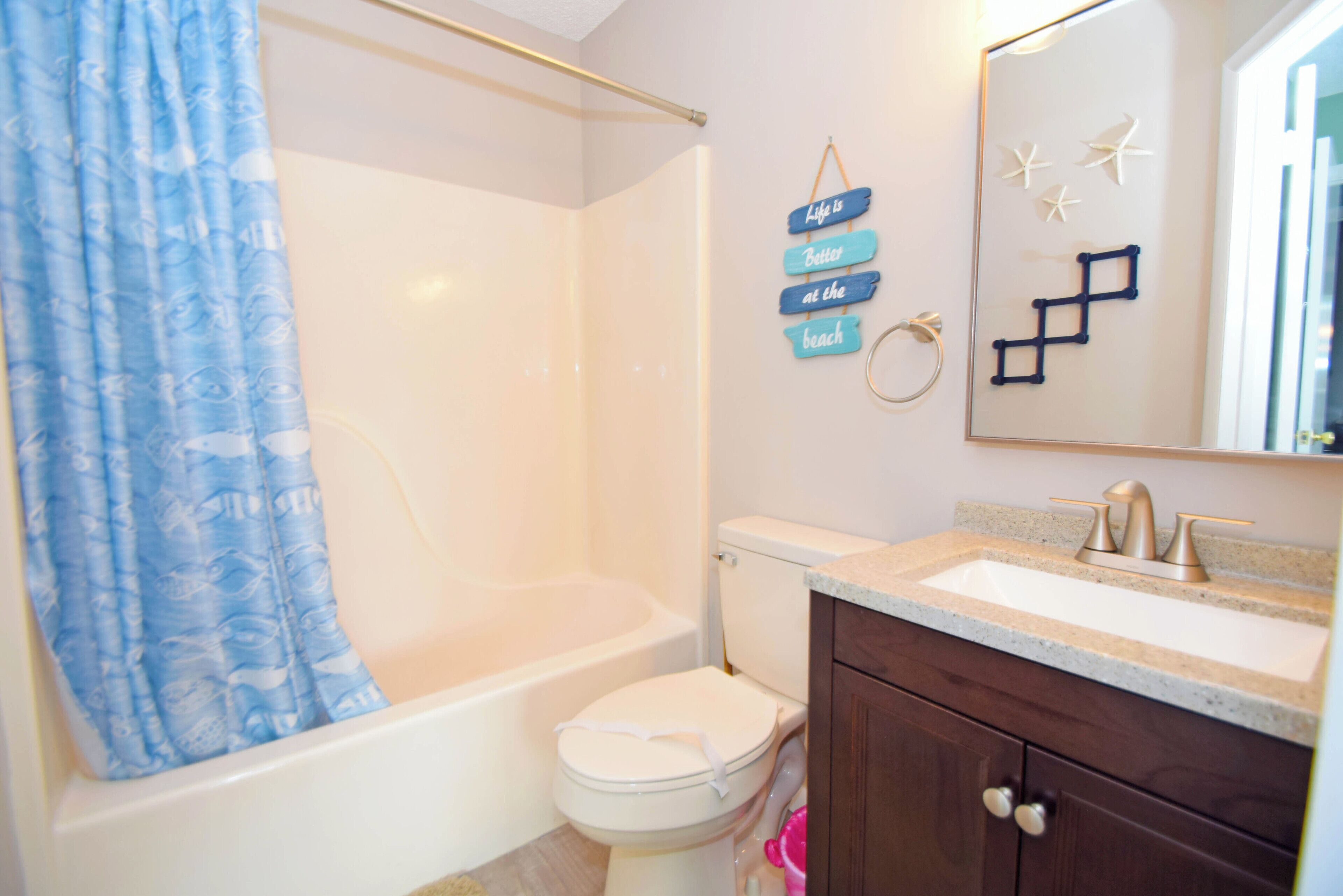 A bathroom with a bathtub, toilet, and vanity with a sink. There is a shower curtain and a wall-mounted sign with text.
