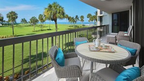 Een balkon met rieten meubels en een tafel voor twee, met uitzicht op een verzorgd gazon en palmbomen.