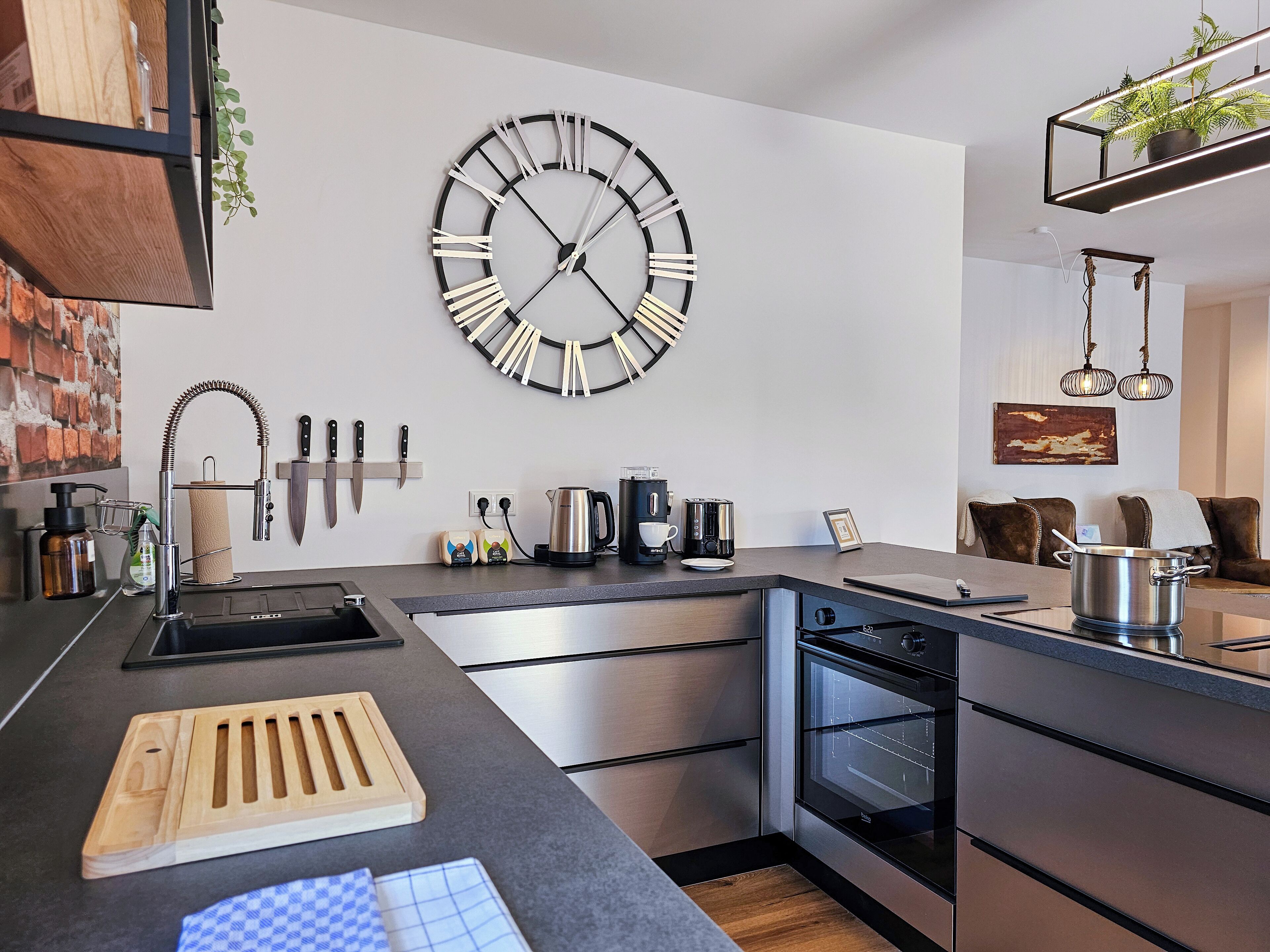 A modern kitchen with a large wall clock, stainless steel appliances, and a wooden cutting board.