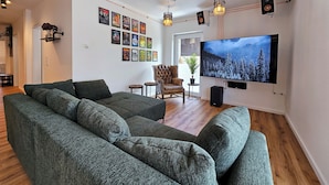Een moderne woonkamer met een grote flatscreen-tv, een donkergroene bank en een muur versierd met filmposters.