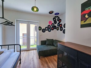 Ein Schlafzimmer mit einem Bett, einem grünen Sofa, Holzboden, einer Deckenleuchte und einer Wand mit Schallplatten.