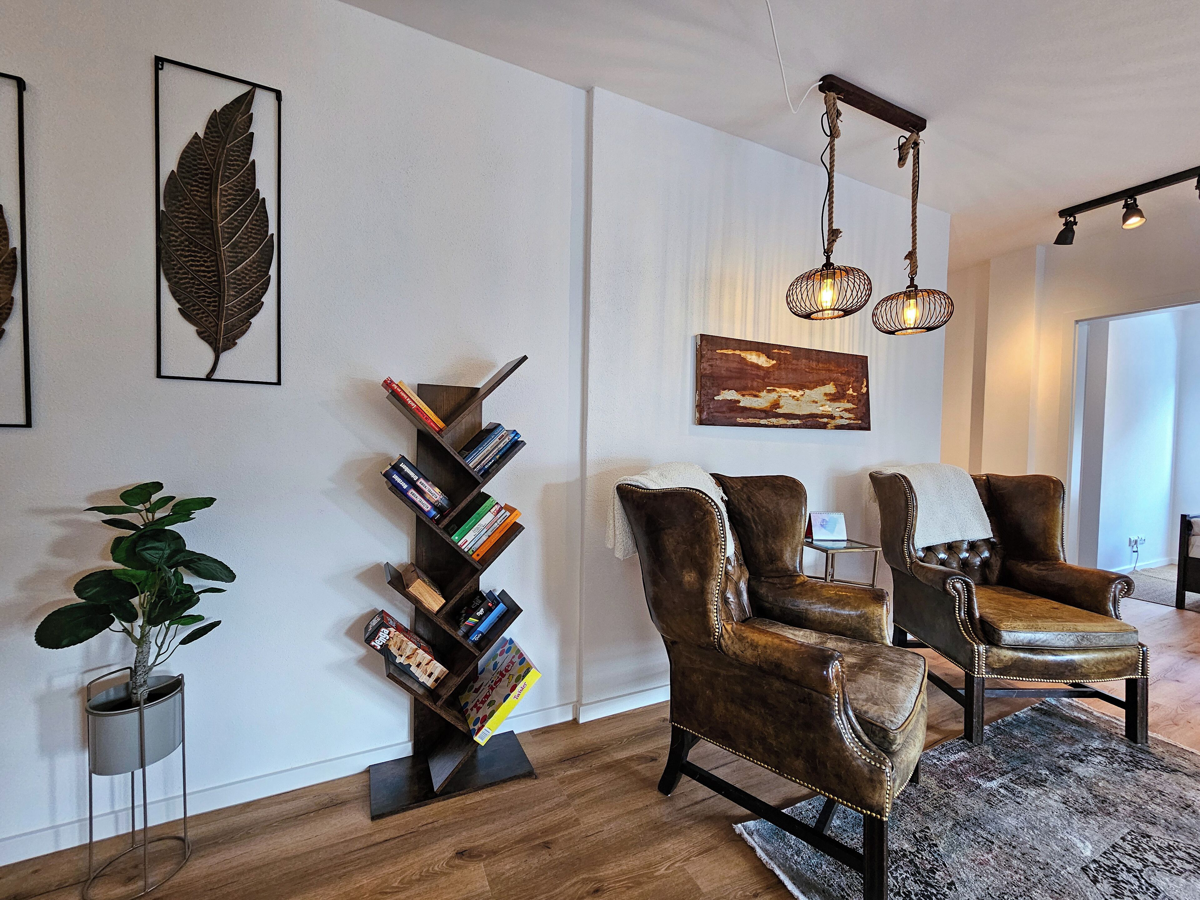 A living room with a bookshelf, two leather armchairs, a plant, and a painting on the wall.