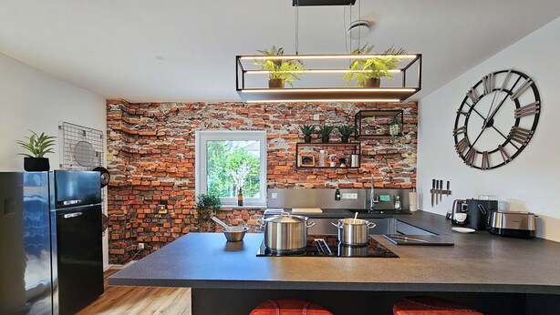 Een moderne keuken met een bakstenen muur, een groot kookeiland met krukken en een klok aan de muur.
