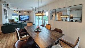 Een moderne woonkamer met een houten eettafel, comfortabele zittingen, een grote flatscreen-tv en een grote spiegel aan de muur.