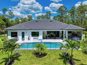 Una casa moderna con una piscina grande, un porche cubierto y vistas a los árboles circundantes.