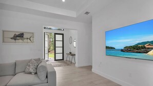 Ett modernt vardagsrum med en stor platt-TV, en soffa och ett inramat konstverk som föreställer fiskar.