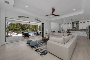 A spacious living area with a large sofa, a coffee table, and a view of a swimming pool and outdoor seating. - Tropical 5-br House With Pool and Outdoor Kitchen (Naples)