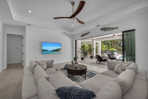 Una sala moderna con un amplio sofá modular, una mesa redonda de centro y un ventilador de techo.