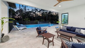 Ett modernt utomhusområde med pool, solstolar, en soffa och en takfläkt.
