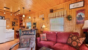 A cozy cabin interior with a red sofa, wooden walls, a kitchen area, and a dining table.