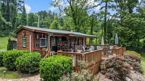 A rustic cabin with a deck, surrounded by lush greenery and a stone pathway.