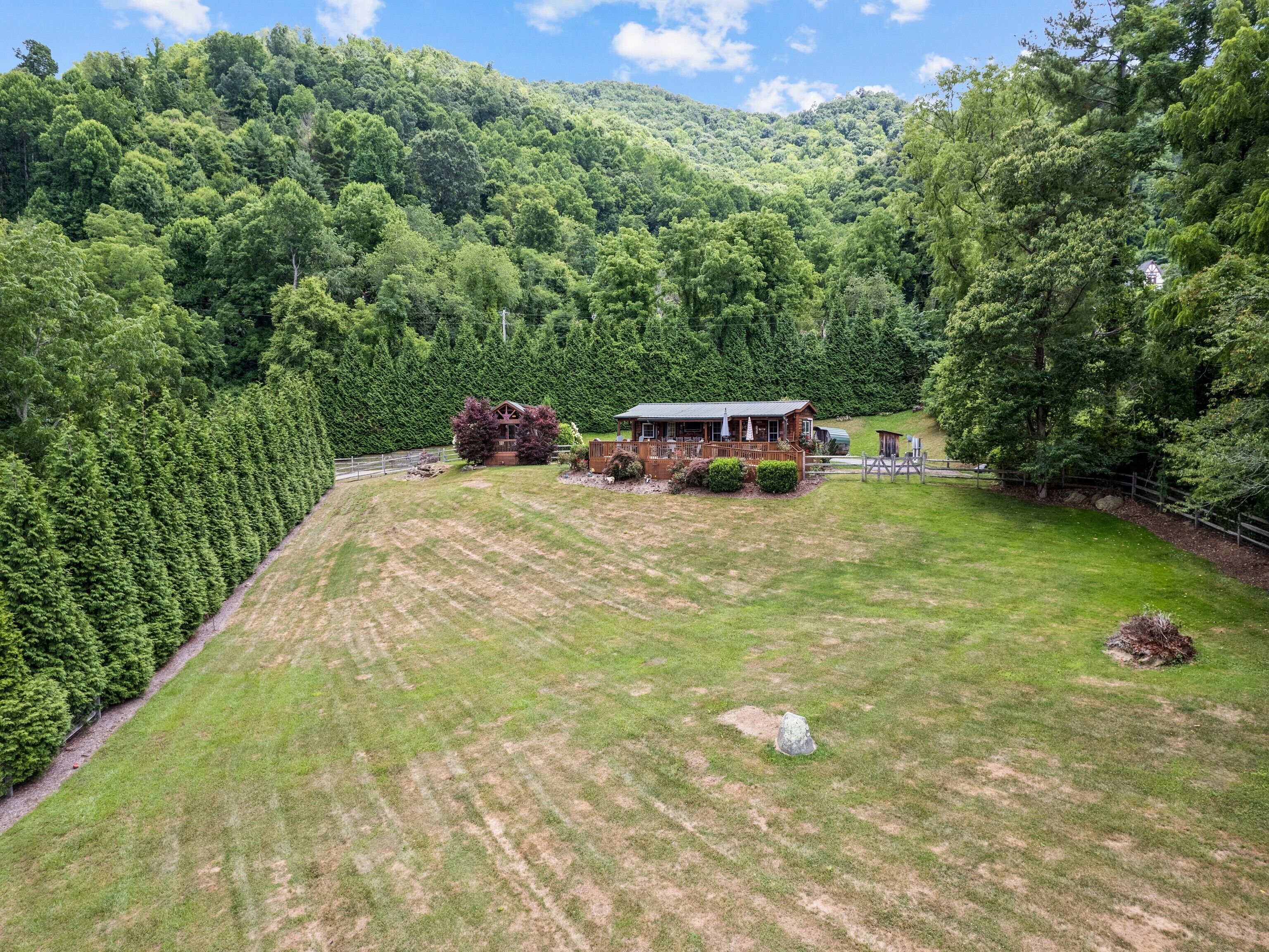 A rural property with a large grassy field, a wooden cabin, and a fenced area with dense forest in the background.