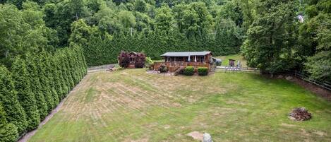 A rural property with a large grassy field, a wooden cabin, and a fenced area with dense forest in the background.