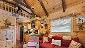 Un acogedor interior de cabaña con paredes de madera, un sofá rojo, un sillón pequeño, una mesa de comedor de madera y una zona de cocina.