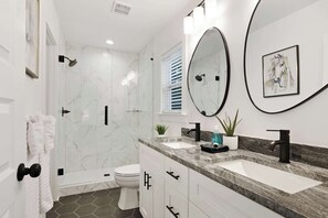 A modern bathroom with a glass-enclosed shower, two sinks, a toilet, and a large mirror. - East Lake Escape | Quick Ride to Decatur & Atlanta (Atlanta)
