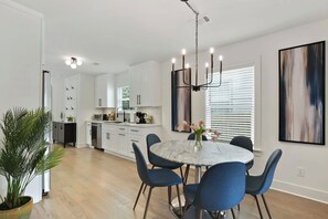 A modern kitchen with white cabinets, a dining area with a marble table and blue chairs, and a large abstract painting on the wall. - East Lake Escape | Quick Ride to Decatur & Atlanta (Atlanta)