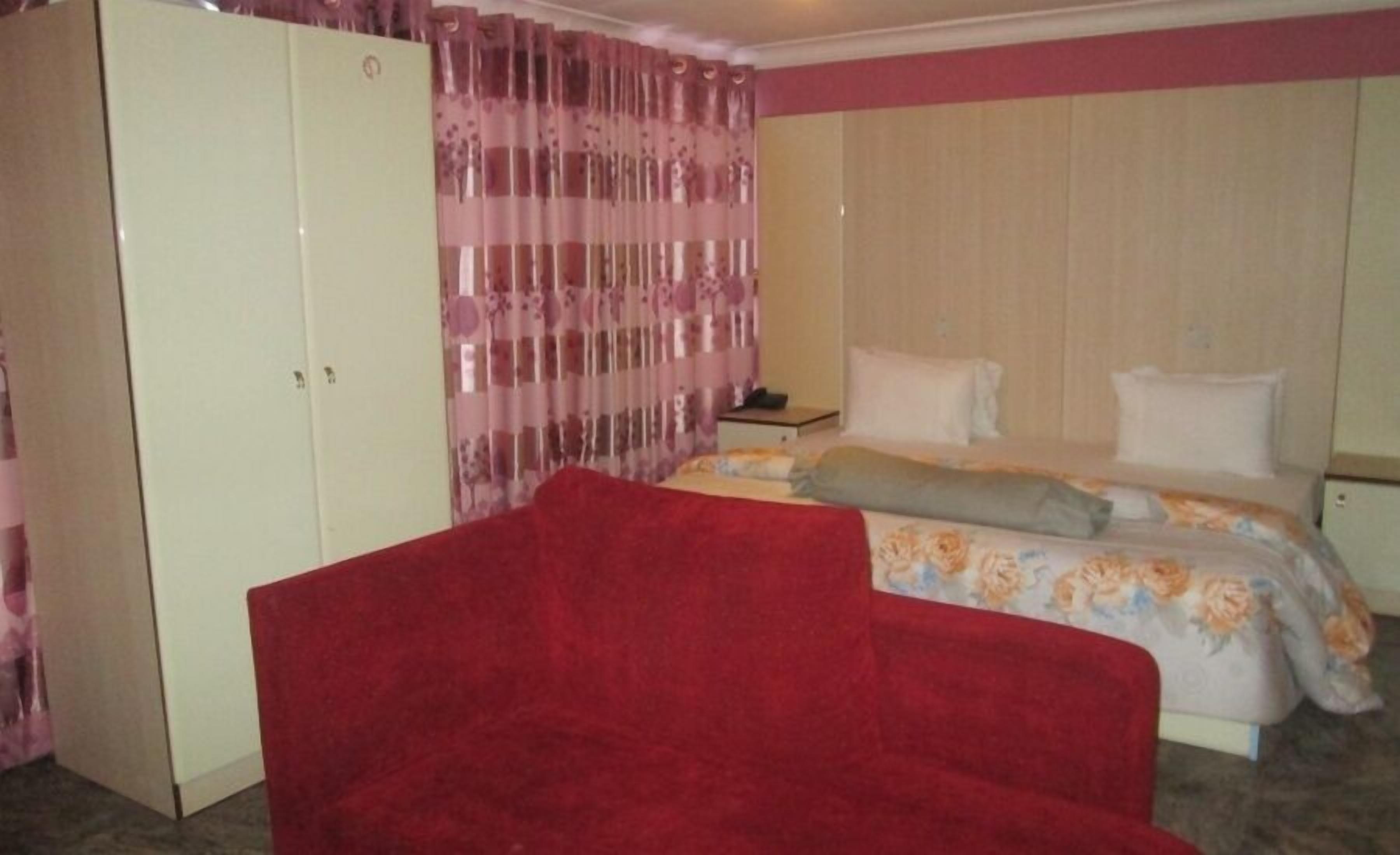 Un dormitorio con cama, una silla roja, un armario y una cortina.
