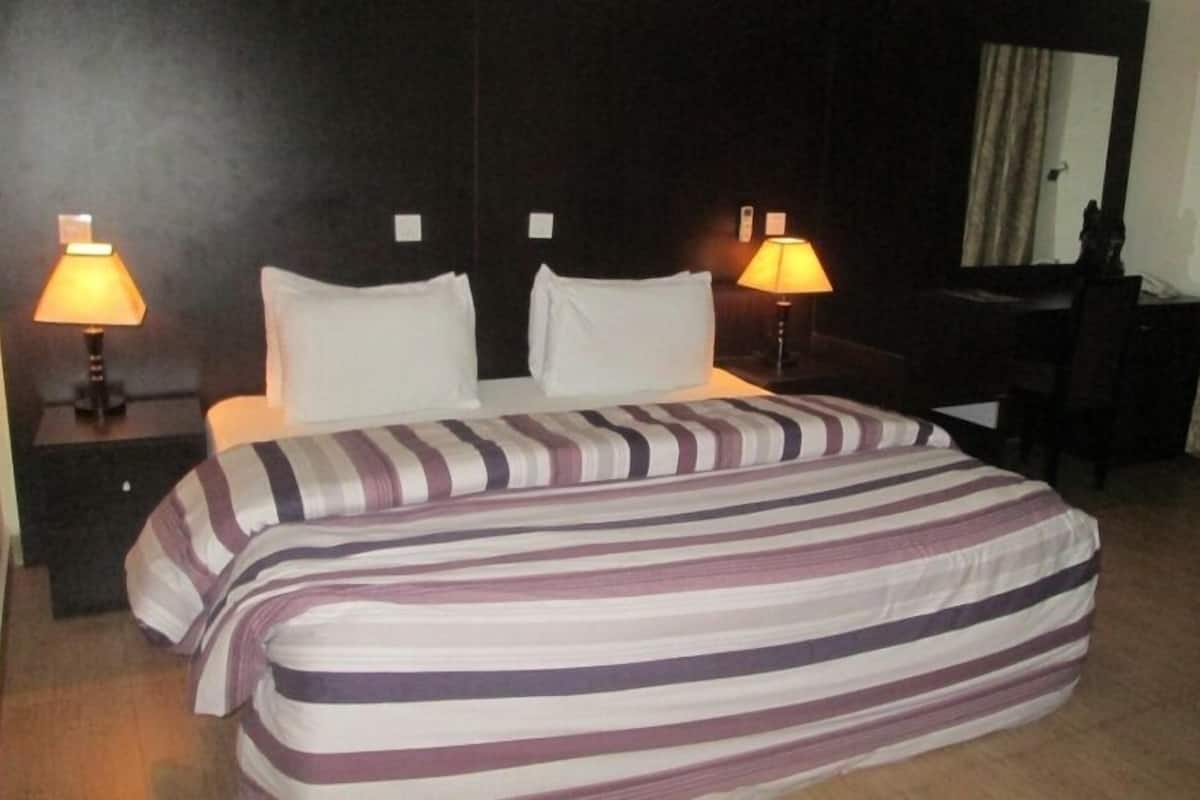 A hotel room with a bed, two bedside lamps, a desk, and a chair.