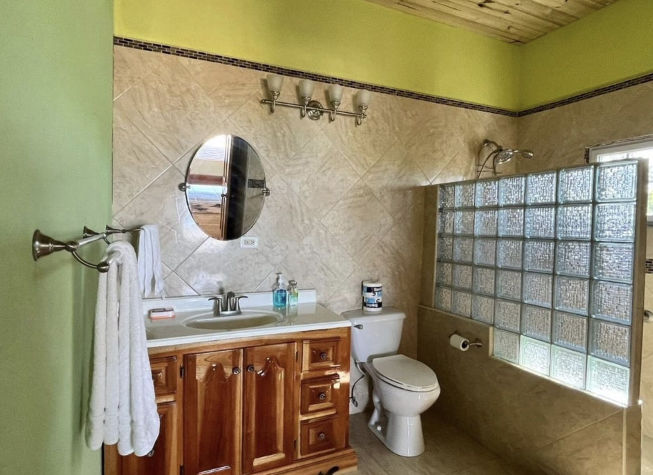 Un baño con tocador de madera, espejo redondo, inodoro y ducha con paneles de vidrio.
