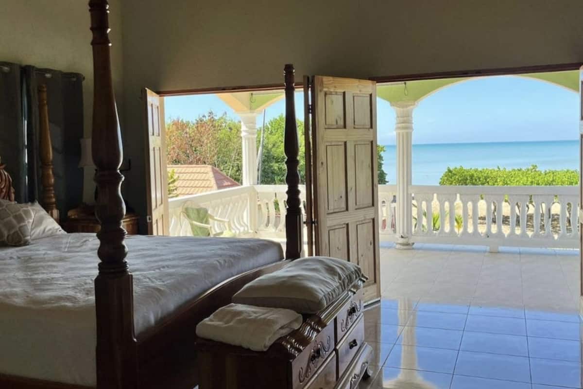 A bedroom with a four-poster bed, a dresser, and a view of the sea through an open door.