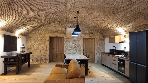 A rustic kitchen with stone walls, a wooden dining table, and a sofa. - LUXURY DIMORA CANELLES (Cagliari)