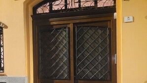 A double wooden door with a diamond-patterned glass window, set in a yellow building with a stone base. - LUXURY DIMORA CANELLES (Cagliari)