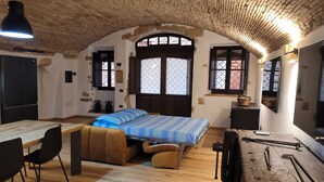 A room with a wooden ceiling, a bed with blue bedding, a desk with chairs, and a window with a view. - LUXURY DIMORA CANELLES (Cagliari)