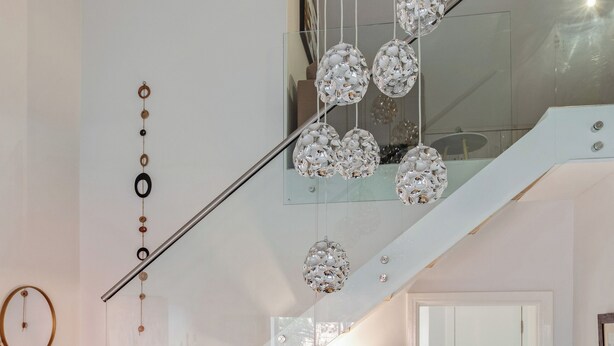 Un interior moderno con una escalera, barandilla de vidrio y esferas de cristal decorativas.