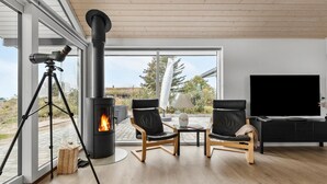 Una sala de estar moderna con una estufa de leña, dos sillones de cuero, un televisor y un telescopio sobre un trípode.