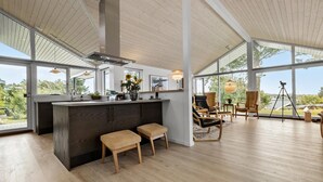 Una cocina moderna con una isla grande, taburetes de madera y vistas al exterior a través de amplios ventanales.