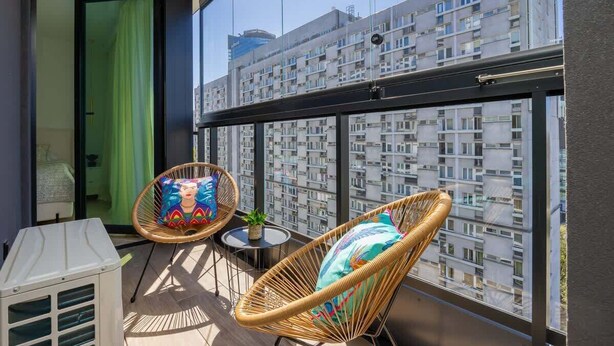 Un balcon avec des fauteuils en osier, une petite table et un radiateur blanc.