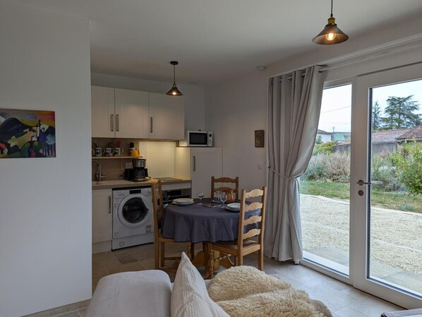 Een compacte keuken met een wasmachine, magnetron en een eethoek met een tafel gedekt voor twee personen.