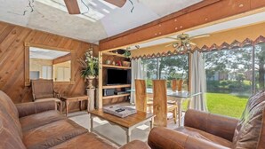A spacious living room with leather sofas, a wooden ceiling, a television, and a large window with a view of the outdoors. - Sandy Beaches *Heated Pool* Pet Friendly (Destin)