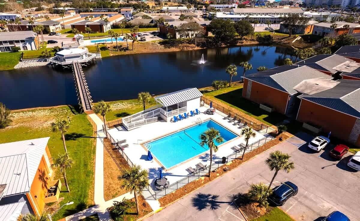 An aerial view of a residential area with a swimming pool, dock, and nearby buildings.