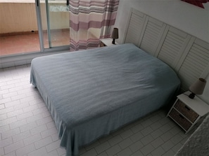 A bedroom with a bed, a nightstand, a lamp, and a window with curtains. - 2-room apartment with terrace 500m from shops, private parking (Port Camargue)
