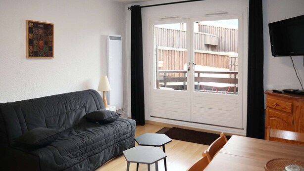 A modern living room with a black sofa, a small table, and a TV on a wooden cabinet. - Ski-in/ski-out studio, Les Orres 1650 center, 4 people (Les Orres)
