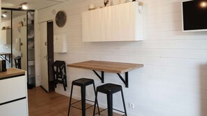 A modern kitchen with a wooden table and two black stools, white cabinetry, and a mounted TV.