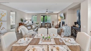 A dining area with a round table set for four, surrounded by chairs. There is a sofa and a television in the background. - Desert Getaway- Private pool, access to PB & fitness centre! (Indio)