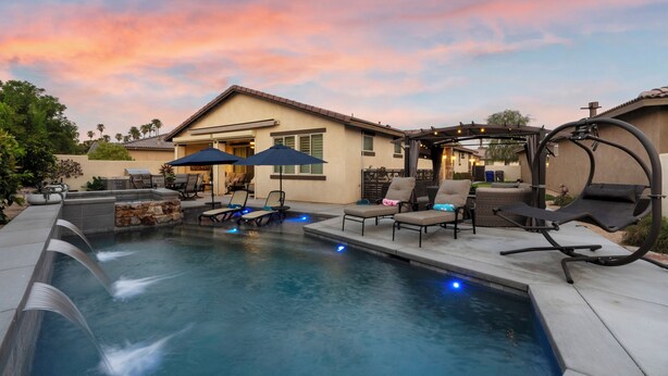 A backyard with a swimming pool, lounge chairs, and a covered patio area. - Desert Getaway- Private pool, access to PB & fitness centre! (Indio)