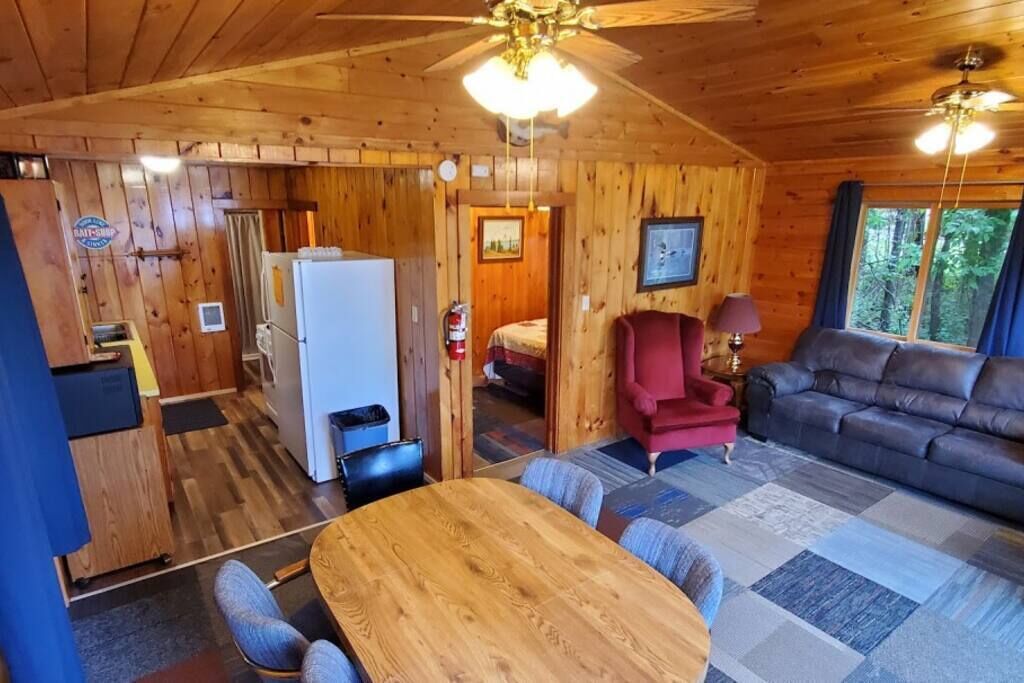 A wooden cabin interior with a dining area, kitchen, and living room.