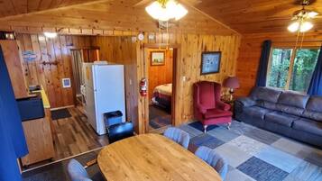 A wooden cabin interior with a dining area, kitchen, and living room.