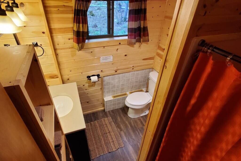 Une salle de bain rustique, aménagée dans une cabane en bois, avec des toilettes, un lavabo et une fenêtre.