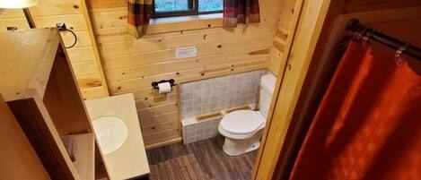 Une salle de bain rustique, aménagée dans une cabane en bois, avec des toilettes, un lavabo et une fenêtre.
