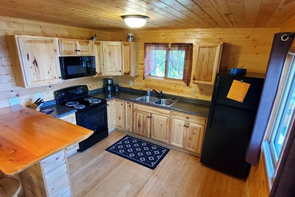 A wooden cabin kitchen with a stove, microwave, sink, and refrigerator.