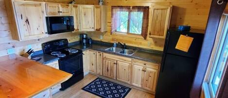 A wooden cabin kitchen with a stove, microwave, sink, and refrigerator.