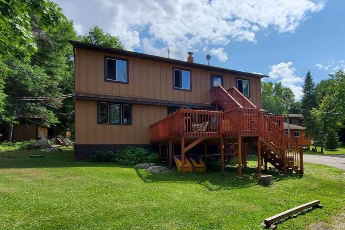 Une maison en bois à deux étages, dotée d’une terrasse en bois et d’un escalier menant à un balcon.