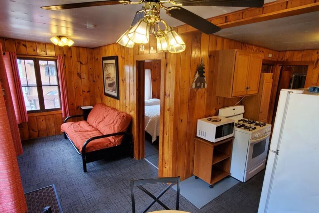 A compact room with a bed, kitchenette, and a ceiling fan.