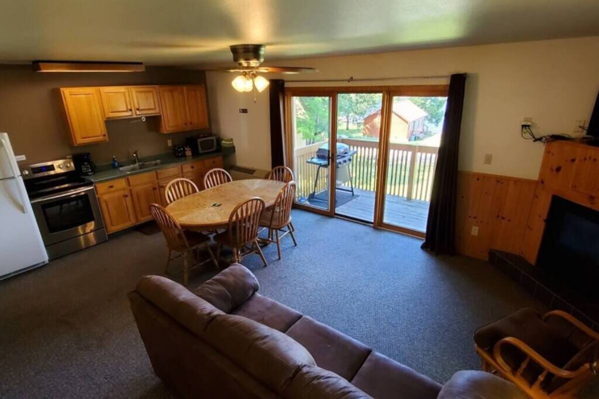 Une cuisine compacte avec des meubles en bois, une table à manger avec des chaises, un canapé et une porte-fenêtre coulissante donnant sur un patio extérieur.