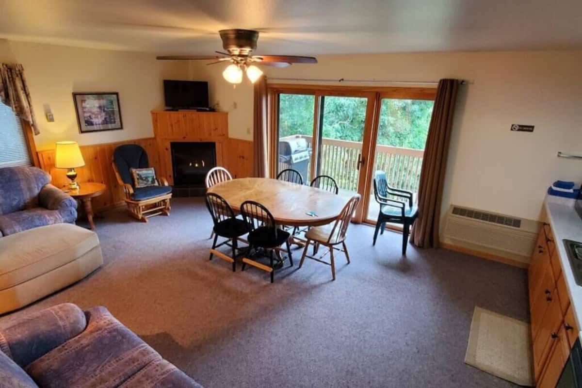 Un salon chaleureux avec une cheminée, une table à manger et un ventilateur de plafond.