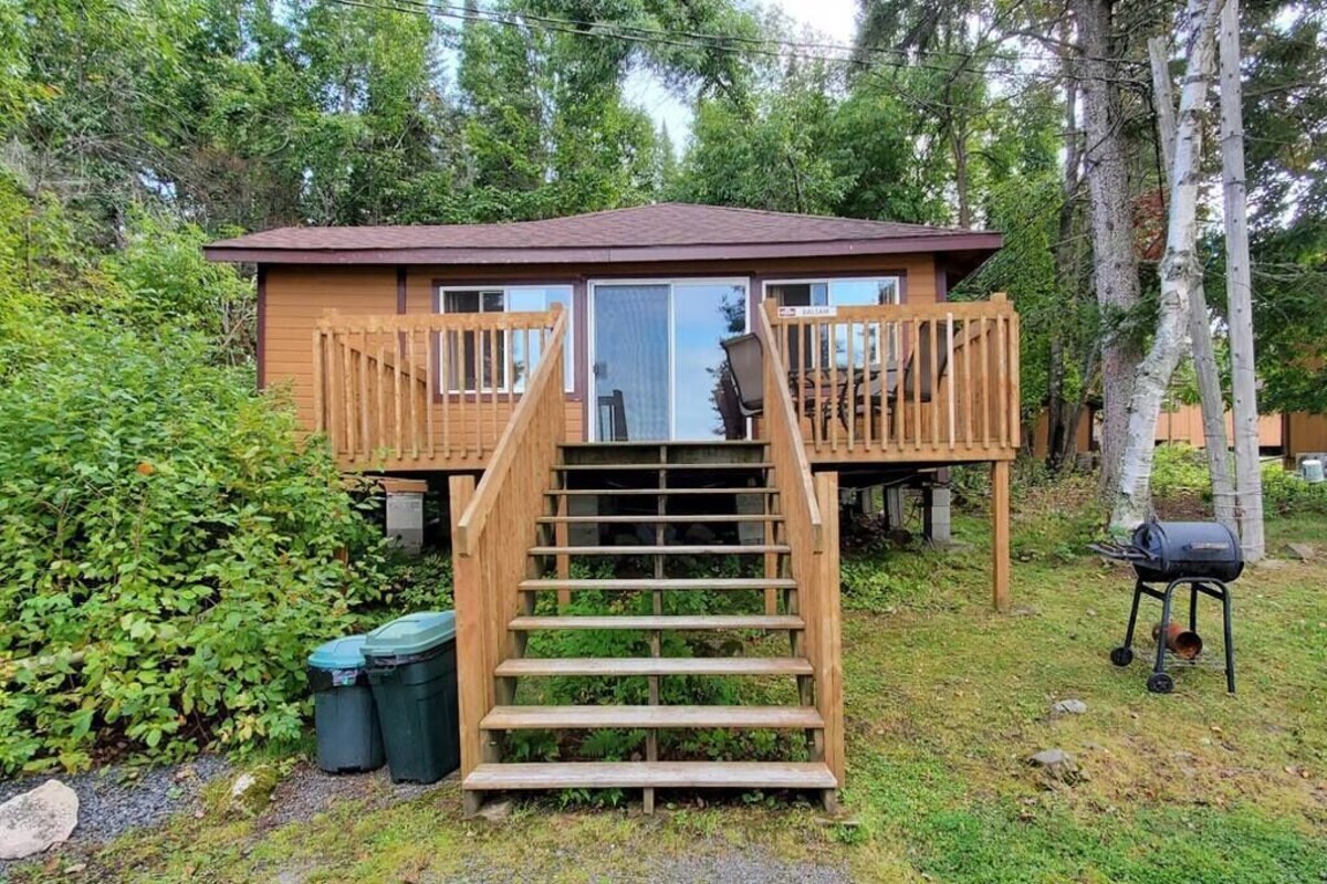 Une cabane dotée d’une terrasse en bois, d’un escalier et d’un barbecue.